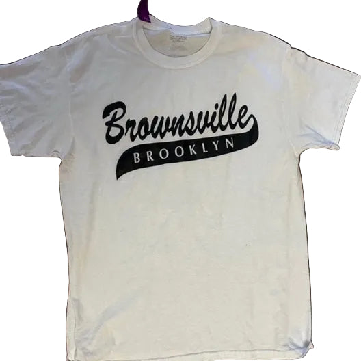 White t-shirt with 'Brownsville Brooklyn' text on a wooden surface