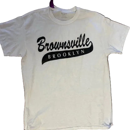 White t-shirt with 'Brownsville Brooklyn' text on a wooden surface
